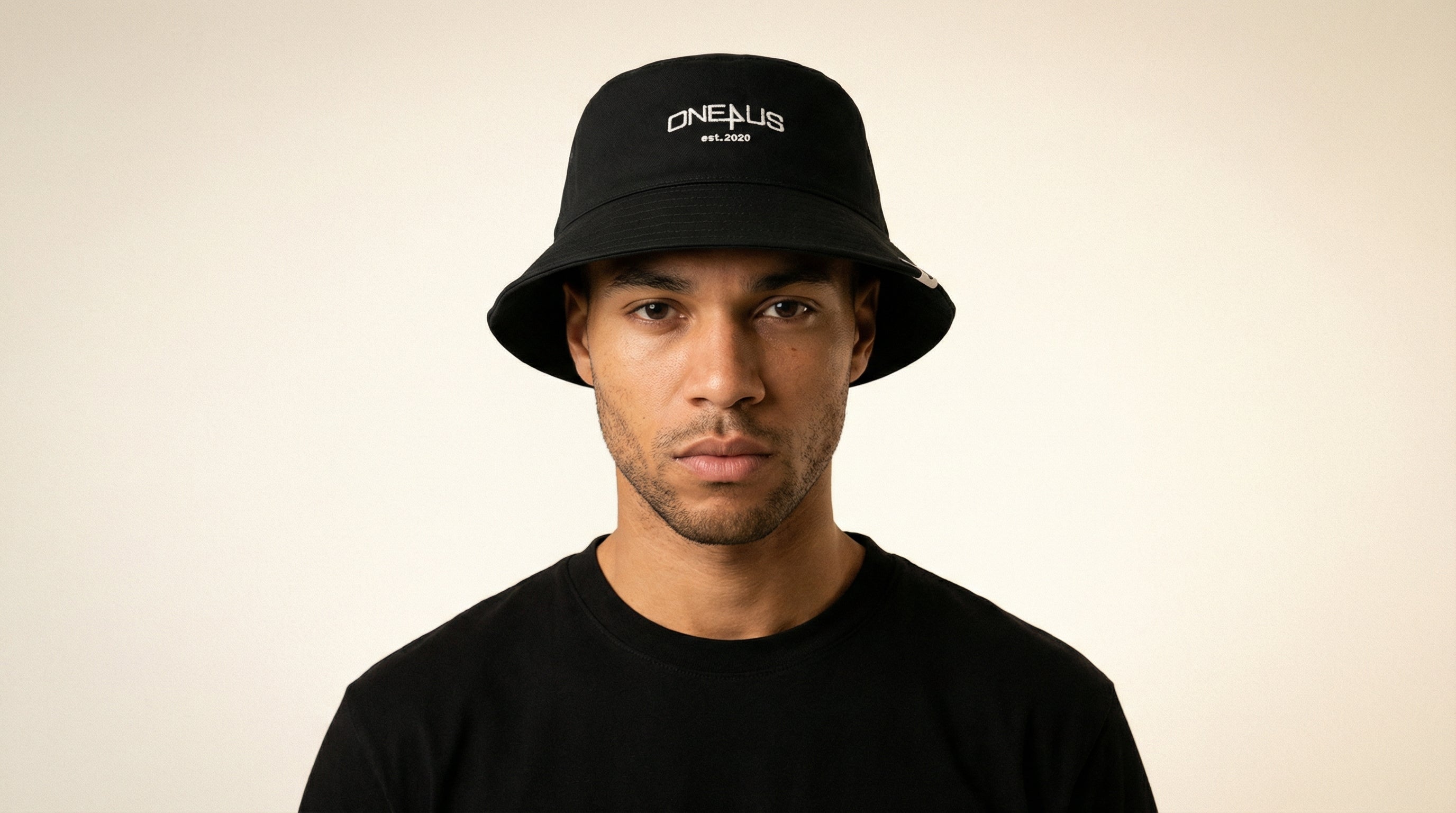 Catalog man wearing a black bucket hat with 'One4Us' branding on a beige background