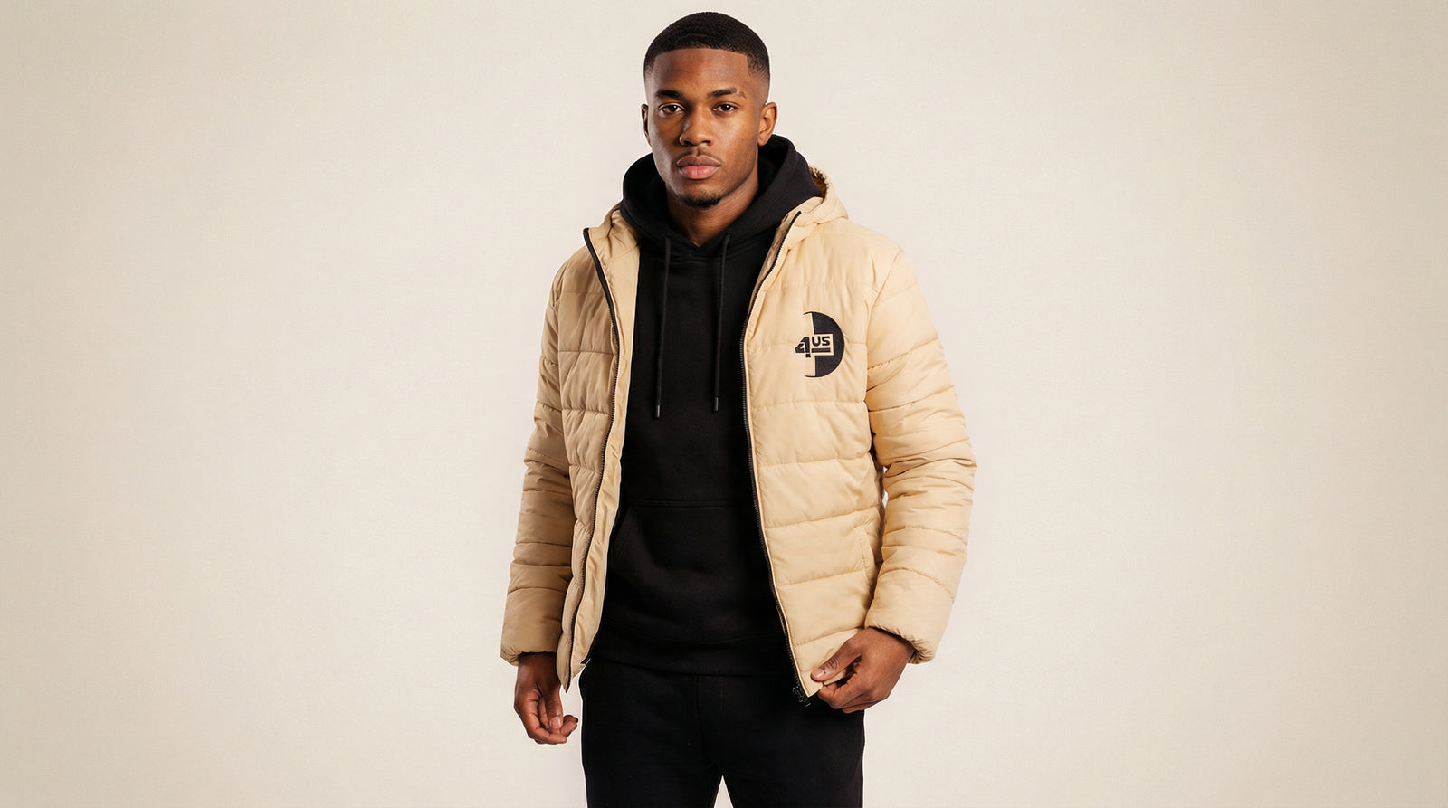 Catalog man wearing a beige puffer jacket over a black hoodie on a beige background