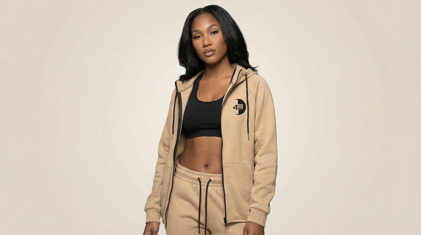 Catalog woman wearing a beige hoodie and black sports bra on a beige background