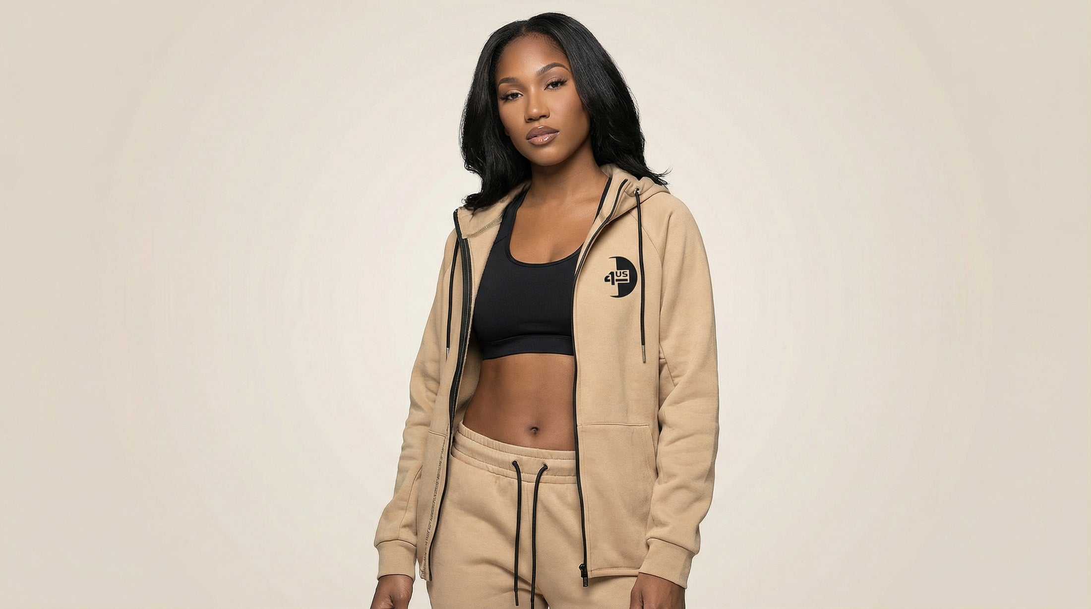Catalog woman wearing a beige hoodie and black sports bra on a beige background