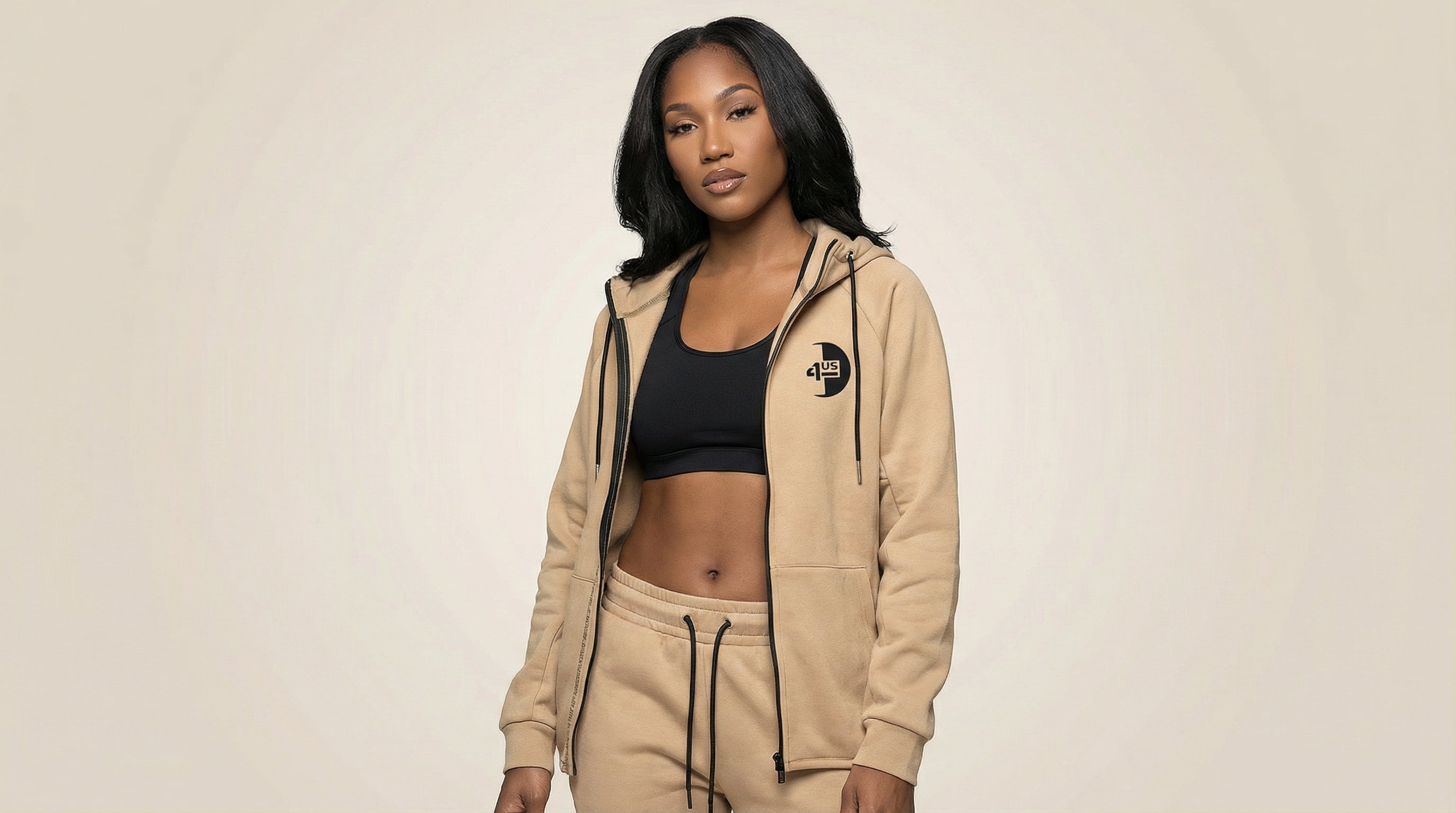 Catalog woman wearing a beige hoodie and black sports bra on a beige background