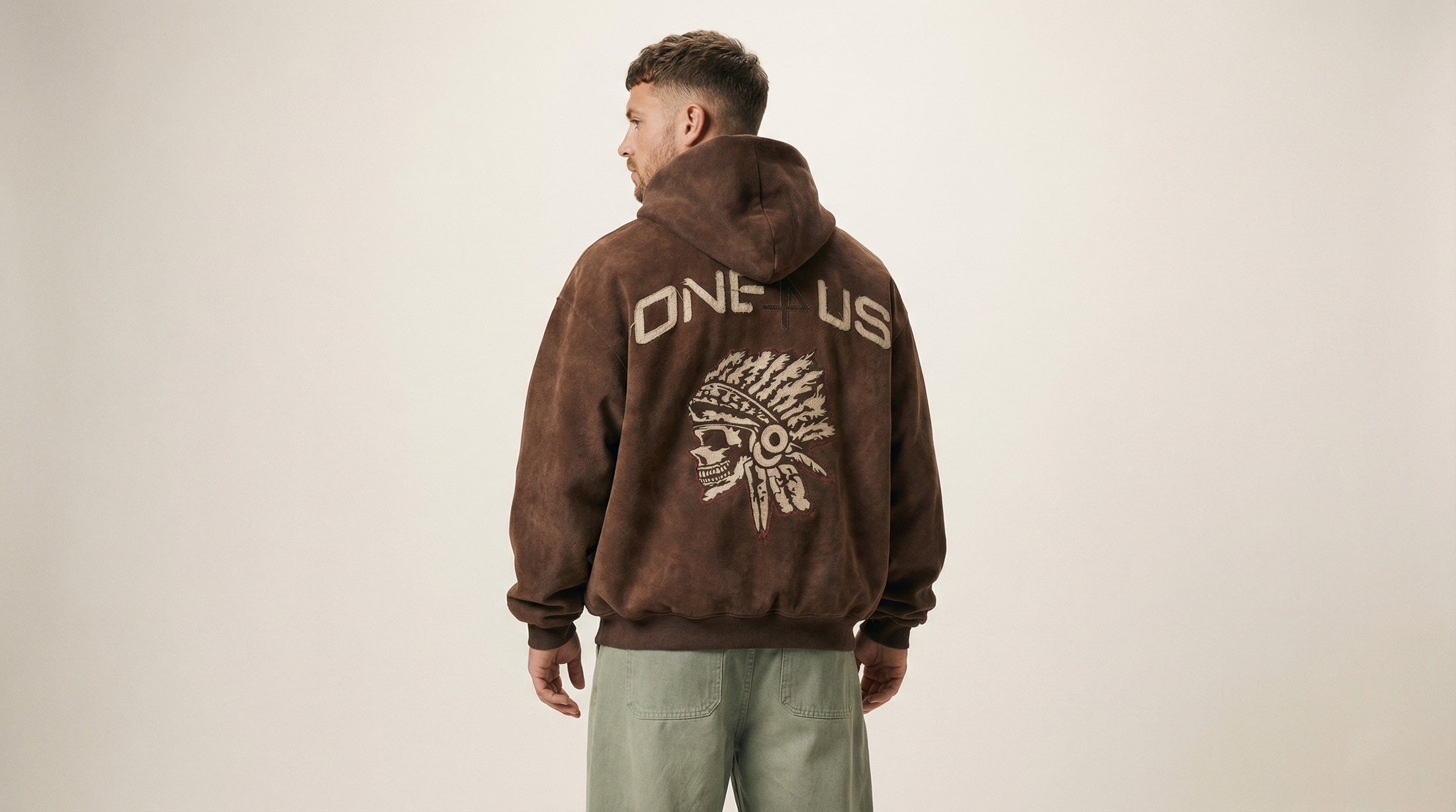 Catalog man wearing a brown hoodie with 'ONE4US' design on the back against a beige background